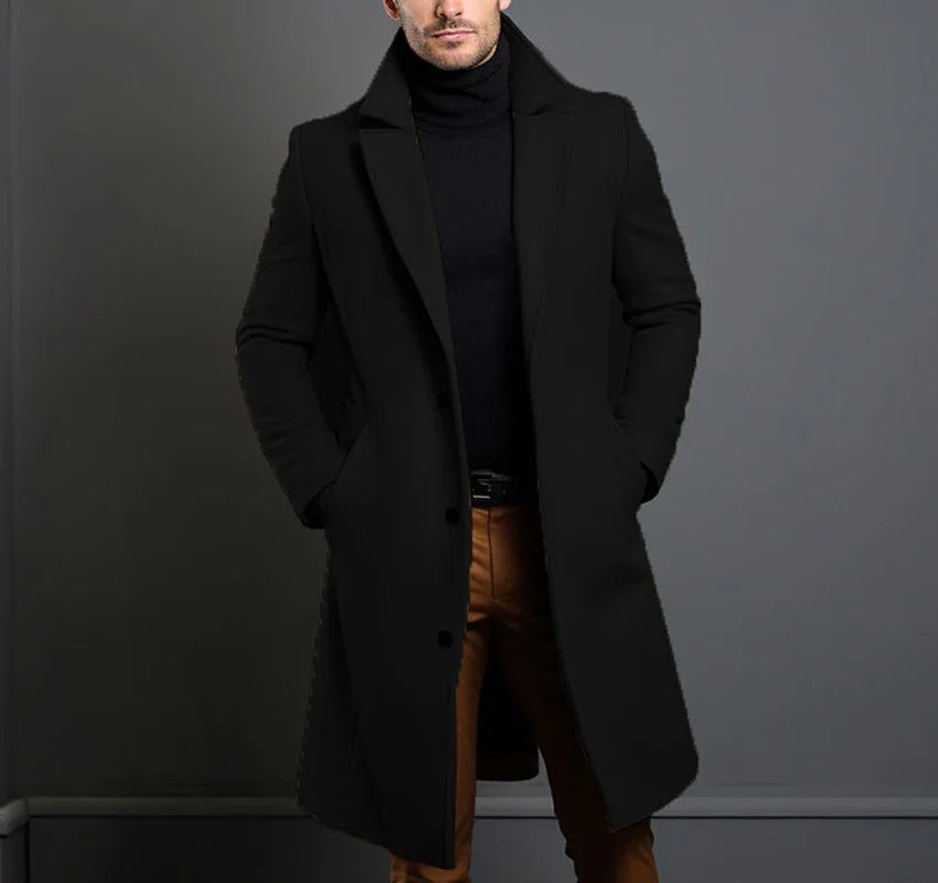 Man wearing black wool overcoat, black turtleneck, and tan pants against grey wall